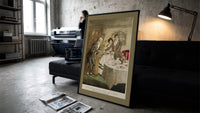 Scrooge visiting nephew at dinner print in a slim black frame leaning on a dark sofa in a concrete print studio