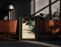 Black-framed Ghostly figure flying over landscape print on a moody console with designer coffee-table books