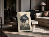 Great blue heron bird print in a black frame leaning on a travertine table in a sunlit lounge