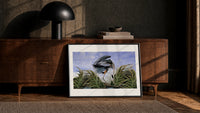 Great blue heron in marsh print in a black frame leaning against a walnut console in lamplight