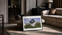 Great blue heron in marsh print in a slim black frame leaning on a travertine coffee table