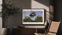 Great blue heron in marsh print in a wood frame above a fluted sideboard beside an olive tree