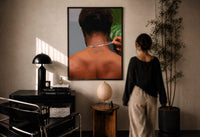 Back View Fastening a Necklace print in a black frame on a sunlit plaster wall, a woman looking on beside a mushroom lamp