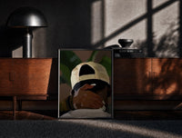 Black-framed Backwards Cap with an Embracing Hand print on the floor in front of a dark wooden console