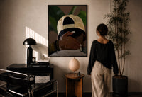 Backwards Cap with an Embracing Hand print in a black frame on a sunlit wall with a viewer