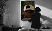 Backwards Cap with an Embracing Hand print in a slim black frame being hung on a sunlit wall in a monochrome room