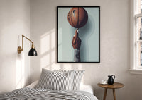 Basketball Balanced on a Fingertip print in a black frame above a bed with striped linens