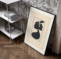 Woman in black gown and hat poster in a black frame leaning beside a shelf in a raw-plaster loft