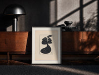Black-framed Woman in black gown and hat print on a moody console with designer coffee-table books