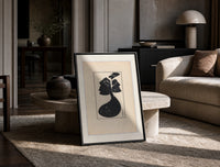 Woman in black gown and hat print in a black frame leaning on a travertine table in a sunlit lounge
