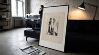 Two Art Nouveau figures embracing print in a slim black frame leaning on a dark sofa in a concrete print studio