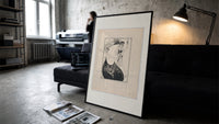 Two elegant women in flowing gowns print in a slim black frame leaning on a dark sofa in a concrete print studio