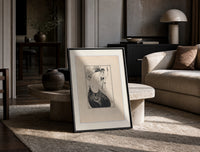 Two elegant women in flowing gowns print in a black frame leaning on a travertine table in a sunlit lounge