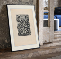 Peacock feather title page design print in a black frame leaning beside a vintage door on parquet