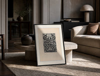 Peacock feather title page design print in a black frame leaning on a travertine table in a sunlit lounge