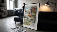 Woman rowing boat on lake print in a slim black frame leaning on a dark sofa in a concrete print studio