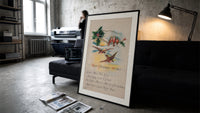 Birds on branch with holly print in a slim black frame leaning on a dark sofa in a concrete print studio