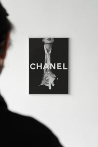 White-framed black and white Chanel fashion wall art on a wall with a silhouetted person in the foreground