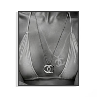 Black and white close-up of a Chanel CC pendant necklace resting over a graffiti-detailed bikini top