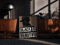 Black-framed Black Is Beautiful Cap print on the floor in front of a dark wooden console