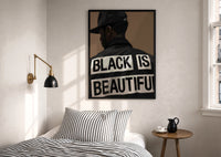 Black Is Beautiful Cap print in a black frame above a bed with striped linens, a brass wall lamp and a sunlit window