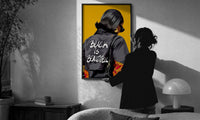 Black Is Beautiful Flame Jacket print in a slim black frame being hung on a sunlit wall in a monochrome room