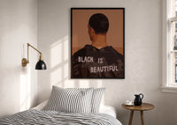 Black Is Beautiful Jacket print in a black frame above a bed with striped linens, a brass wall lamp and a sunlit window