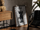Walnut-framed Black KAWS Companion figure standing print leaning against a sunlit rustic brick wall