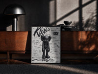Black-framed head-bowed KAWS Companion print on a moody console with designer coffee-table books