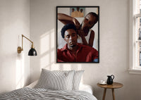 Black Man Having His Hair Braided print in a black frame above a bed with striped linens