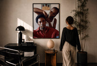Black Man Having His Hair Braided print in a black frame on a sunlit plaster wall, a woman looking on beside a mushroom lamp