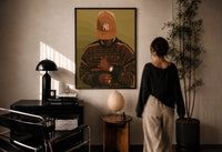Black Man in Brown Baseball Cap print in a black frame on a sunlit plaster wall, a woman looking on beside a mushroom lamp
