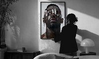 Black Man in Metallic Sunglasses print in a slim black frame being hung on a sunlit wall in a monochrome room