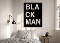 Black Man Lettering print in a black frame above a bed with striped linens, a brass wall lamp and a sunlit window