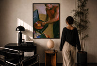 Black Man Playing a Vinyl Record print in a black frame on a sunlit plaster wall, a woman looking on beside a mushroom lamp