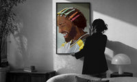 Black Man with Colorful Hair Clips print in a slim black frame being hung on a sunlit wall in a monochrome room