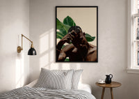 Black Man with Hand on Head print in a black frame above a bed with striped linens, a brass wall lamp and a sunlit window