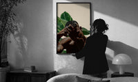 Black Man with Hand on Head print in a slim black frame being hung on a sunlit wall in a monochrome room