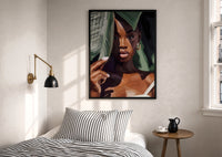Black Woman with Tropical Leaves print in a black frame above a bed with striped linens
