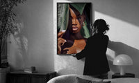 Black Woman with Tropical Leaves print in a slim black frame being hung on a sunlit wall in a monochrome room
