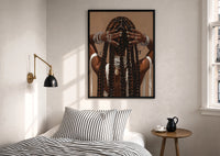 Black Woman Holding Her Braids print in a black frame above a bed with striped linens, a brass wall lamp and a sunlit window