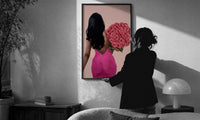 Black Woman Holding Pink Roses print in a slim black frame being hung on a sunlit wall in a monochrome room