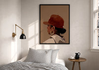 Black Woman in Red Baseball Cap print in a black frame above a bed with striped linens, a brass wall lamp and a sunlit window