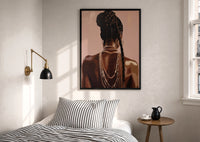 Black Woman with a Braided Bun print in a black frame above a bed with striped linens, a brass wall lamp and a sunlit window