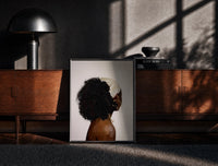 Black-framed Black Woman with a Curly Puff print on the floor in front of a dark wooden console