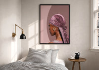 Black Woman with a Pink Headscarf print in a black frame above a bed with striped linens