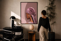 Black Woman with a Pink Headscarf print in a black frame on a sunlit plaster wall, a woman looking on beside a mushroom lamp
