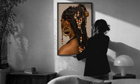 Black Woman with Beaded Braids print in a slim black frame being hung on a sunlit wall in a monochrome room