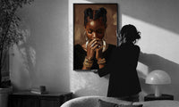 Black Woman with Clasped Hands print in a slim black frame being hung on a sunlit wall in a monochrome room