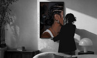 Black Woman with Cornrow Braids print in a slim black frame being hung on a sunlit wall in a monochrome room